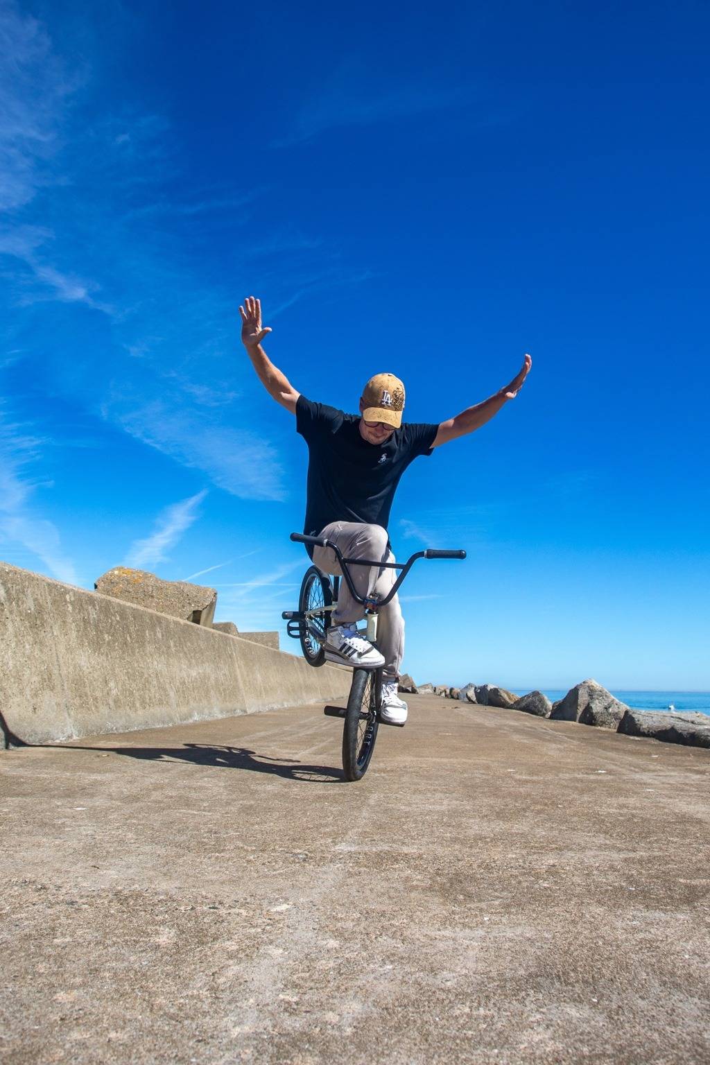 Kevin Meyer en équilibre sur la roue avant de son BMX, bras écartés, en bord de mer