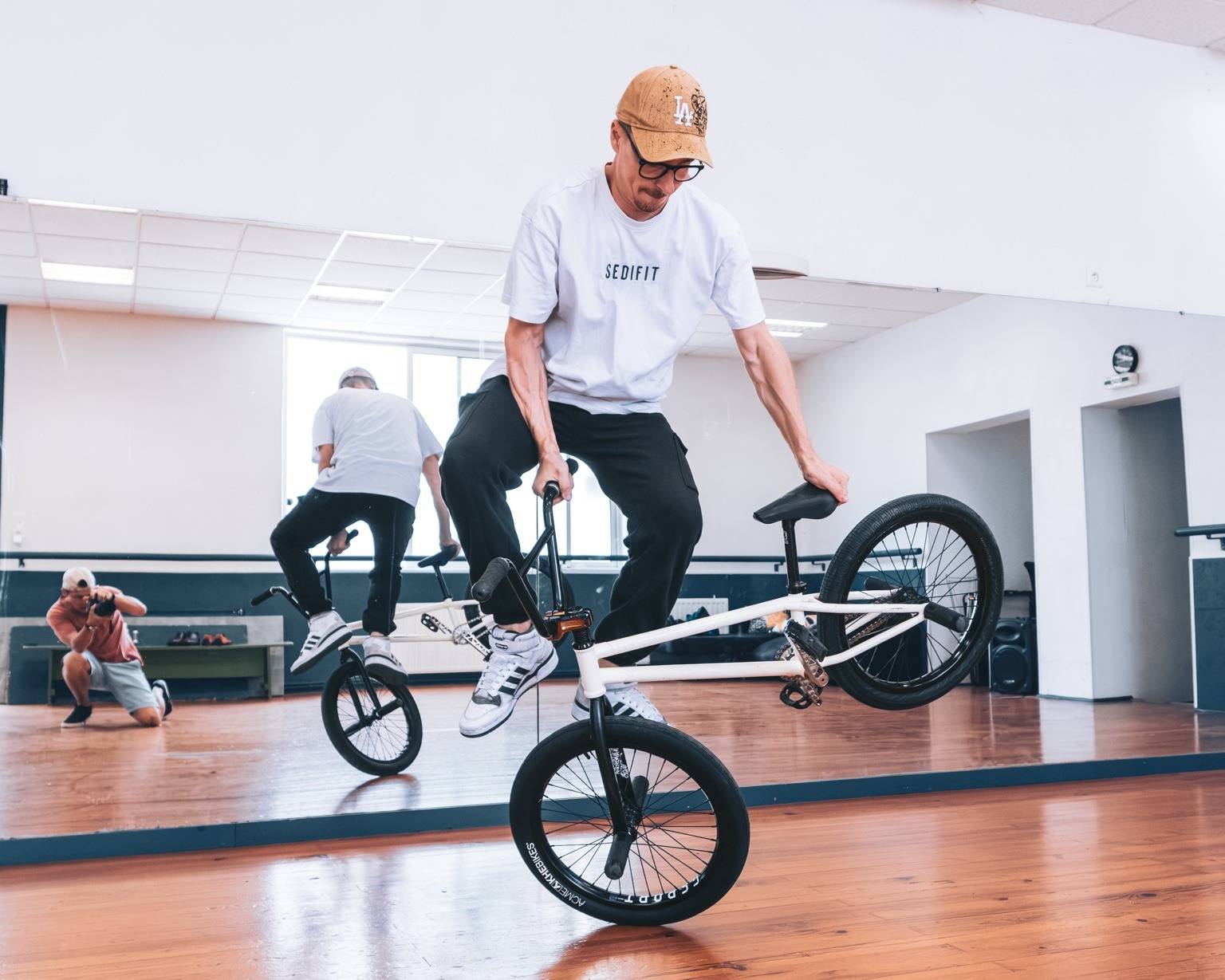 Kevin Meyer en équilibre sur la roue avant de son BMX dans une salle au sol en parquet